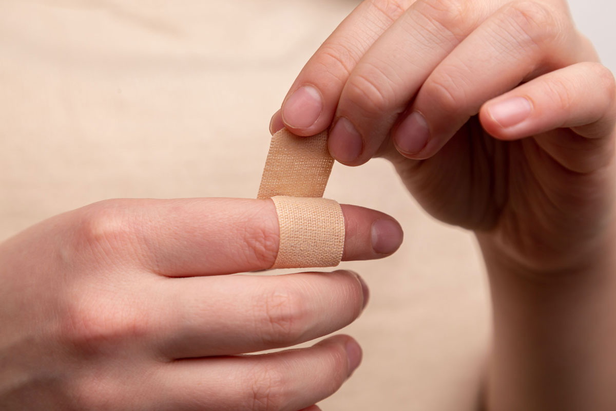 A person putting a bandaid on their finger | Orange Naturals