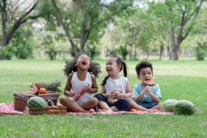 Kids eating watermelon at a park beside a picnic basket