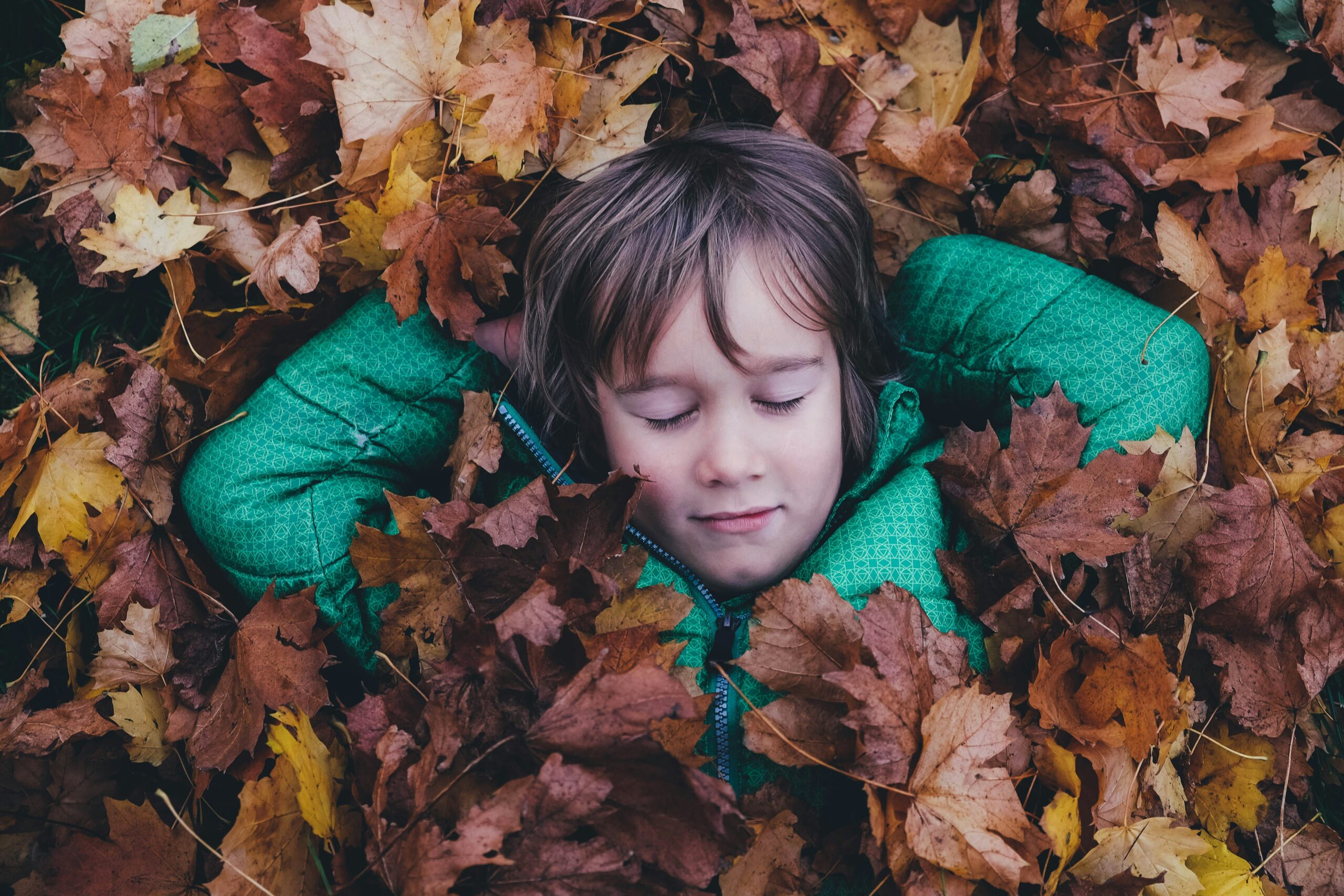 Kid laying in fall leaves with his hands behind his head and his eyes closed