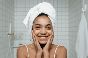Woman smiling, looking in mirror with hair wrapped in towel.