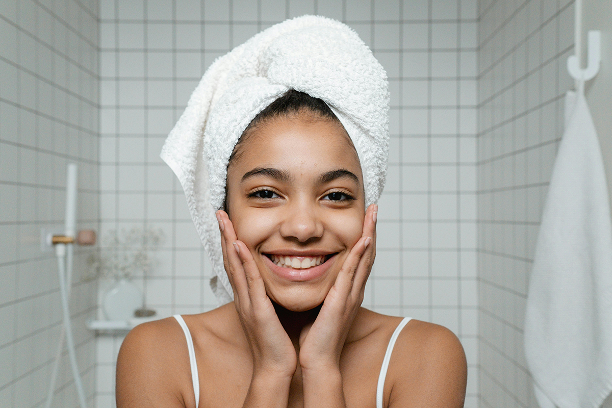 Woman smiling, looking in mirror with hair wrapped in towel.