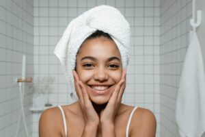 Girl smiling in front of mirror with clean face and hair wrapped in a towel.